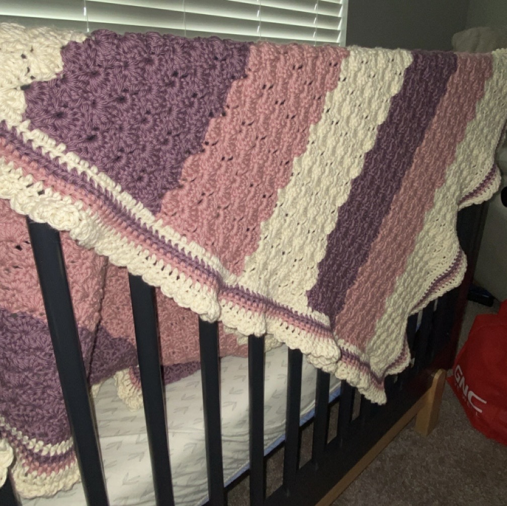 Crocheted baby blanket laying over the edge of a crib