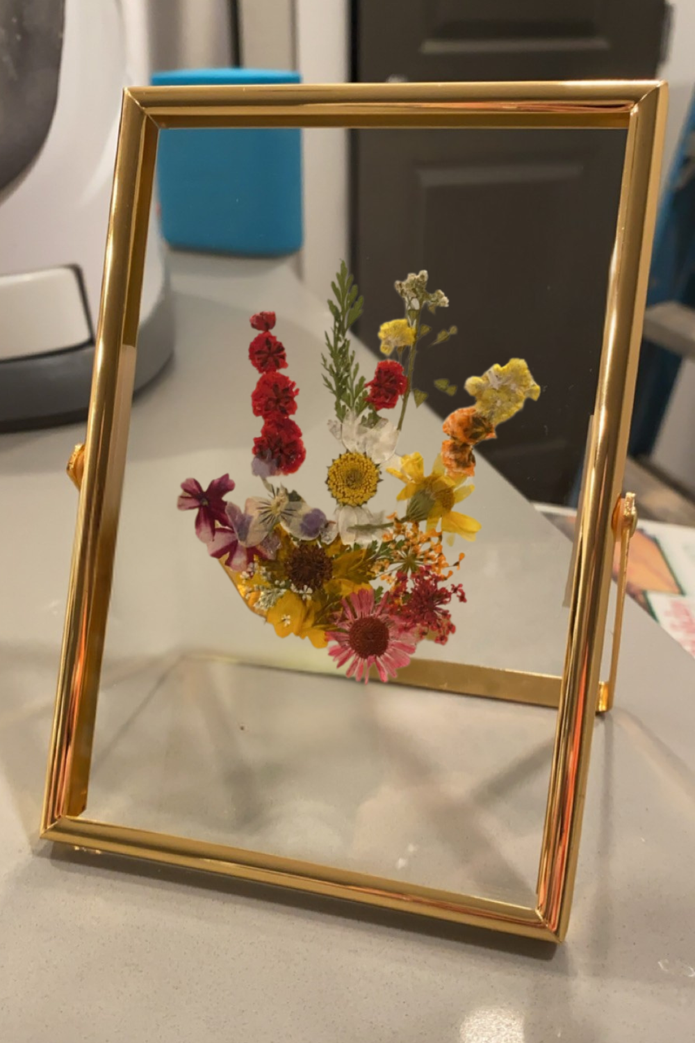 Gold frame with clear glass and a child's handprint made of dried flowers