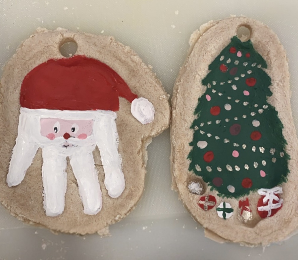 Two Christmas ornaments made of dough with a child's hand and footprints painted to look like Santa Clause and a Christmas tree